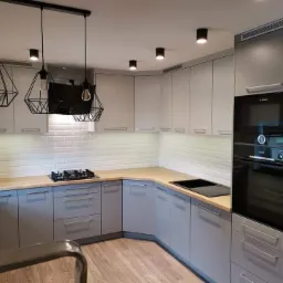 Nowoczesna kuchnia w Brodnicy z szarymi frontami, drewnianymi blatami i geometrycznymi lampami wiszącymi, wykończona białymi płytkami imitującymi cegłę.