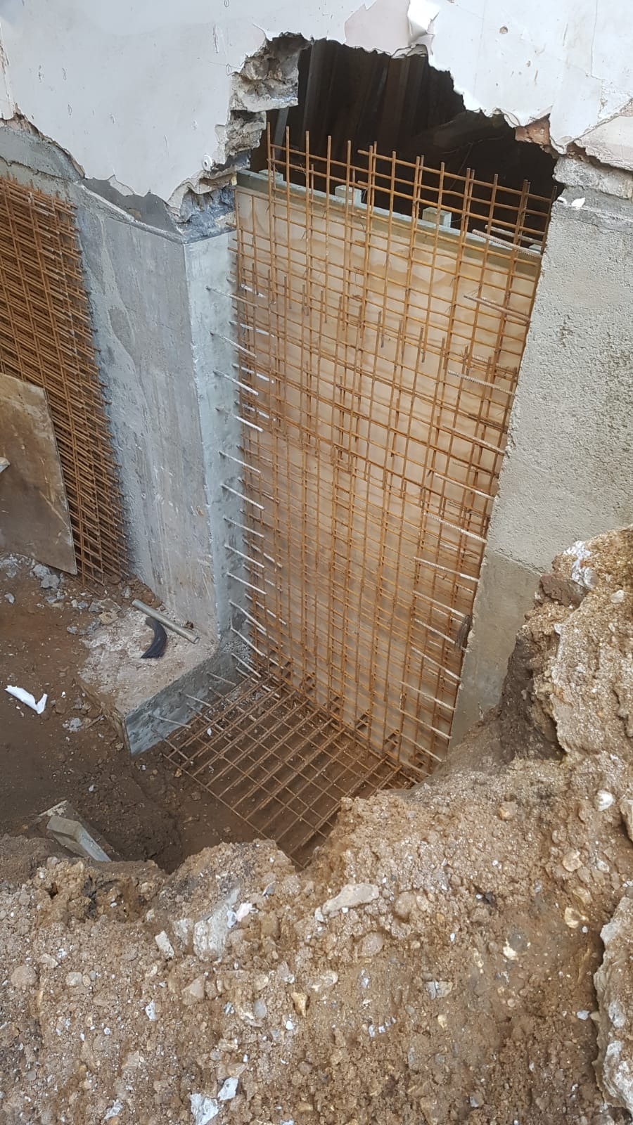 Zbrojenie ze stalowej siatki osadzone w betonowej konstrukcji przy uszkodzonym suficie, widoczny wykop ziemny i resztki gruzu.