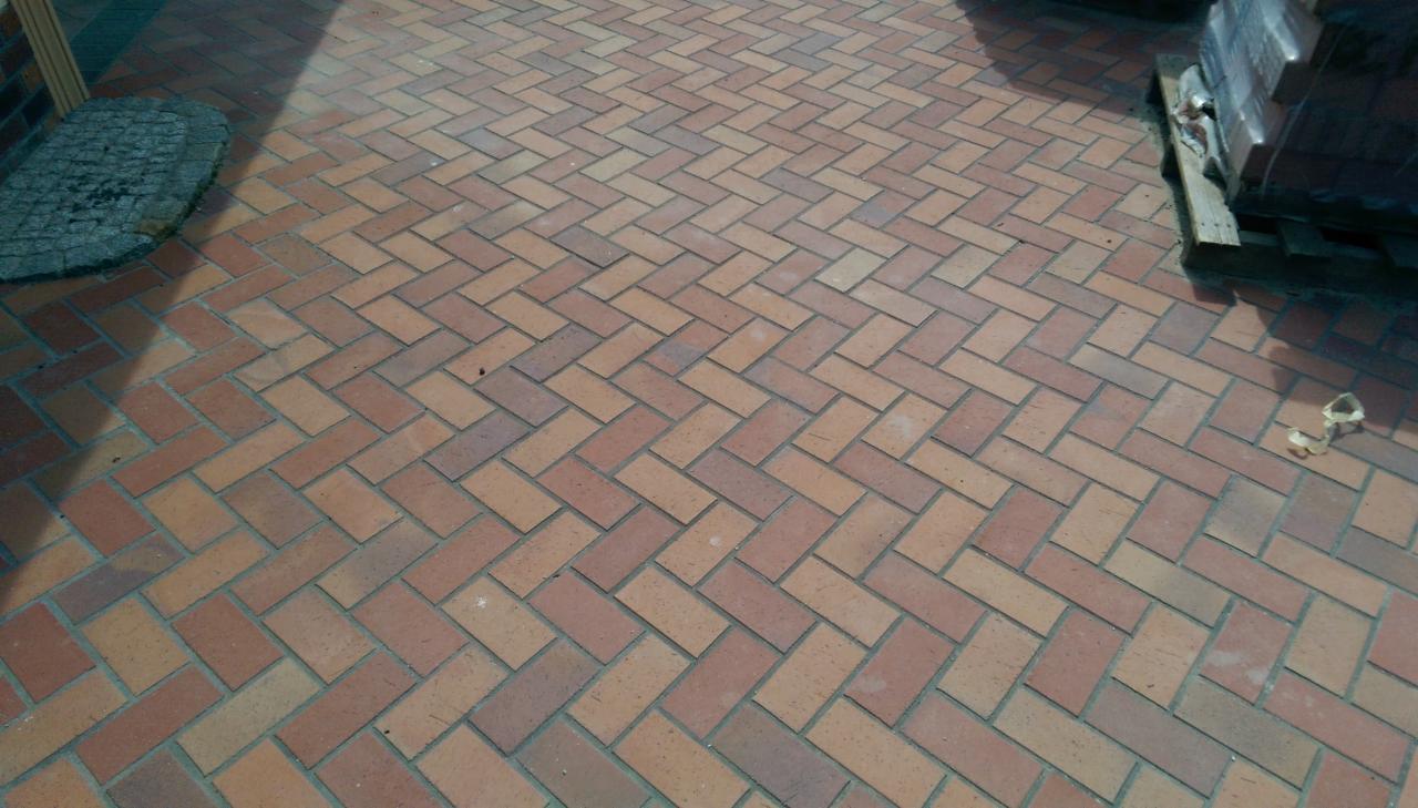 Ułożona kostka brukowa w wzór jodełki, z paletą kostki w tle i drobnymi śmieciami na powierzchni.