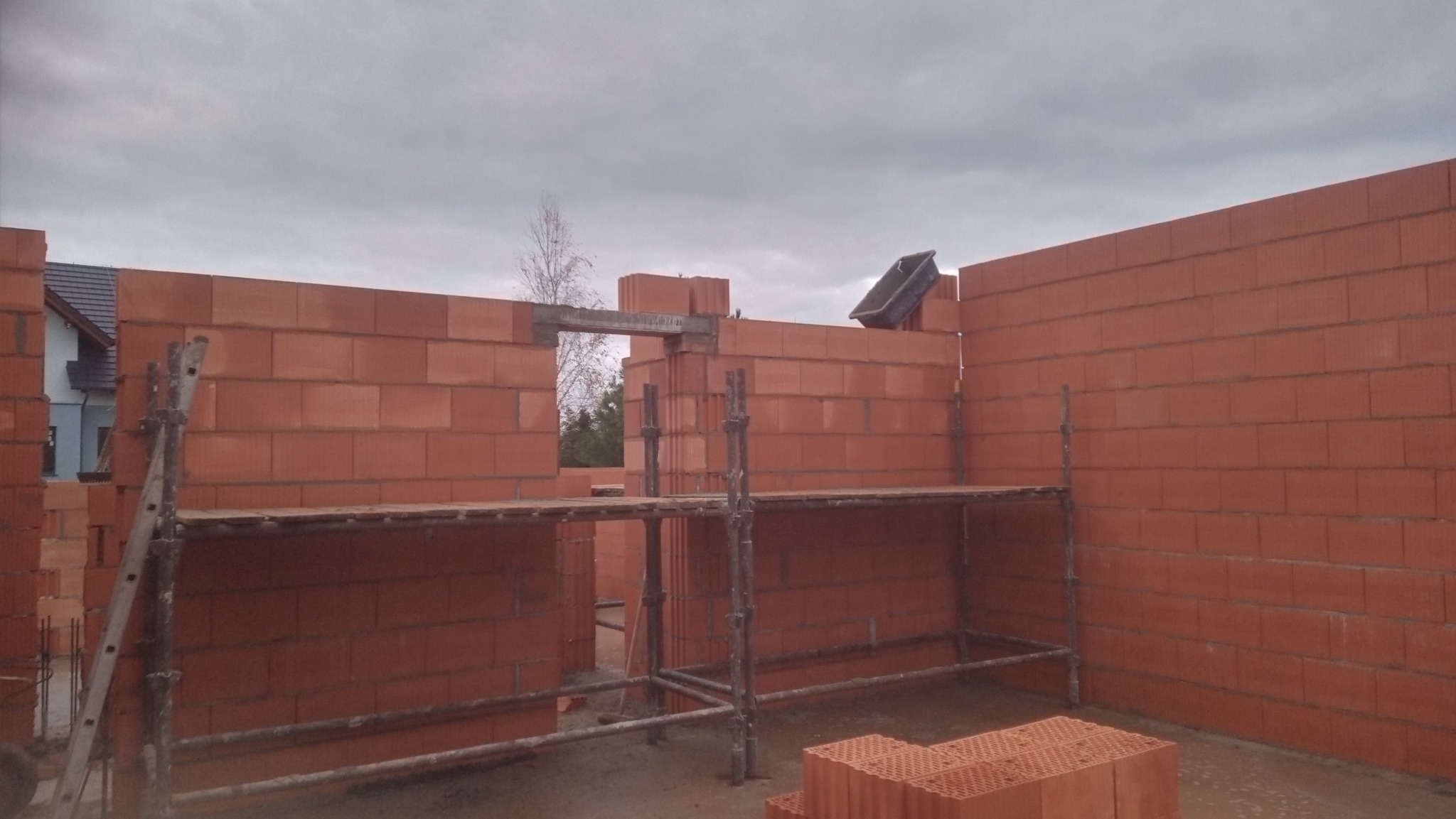 Wznoszenie ścian parteru domu jednorodzinnego w Dopiewie, widoczne rusztowania i pustaki ceramiczne na palecie.