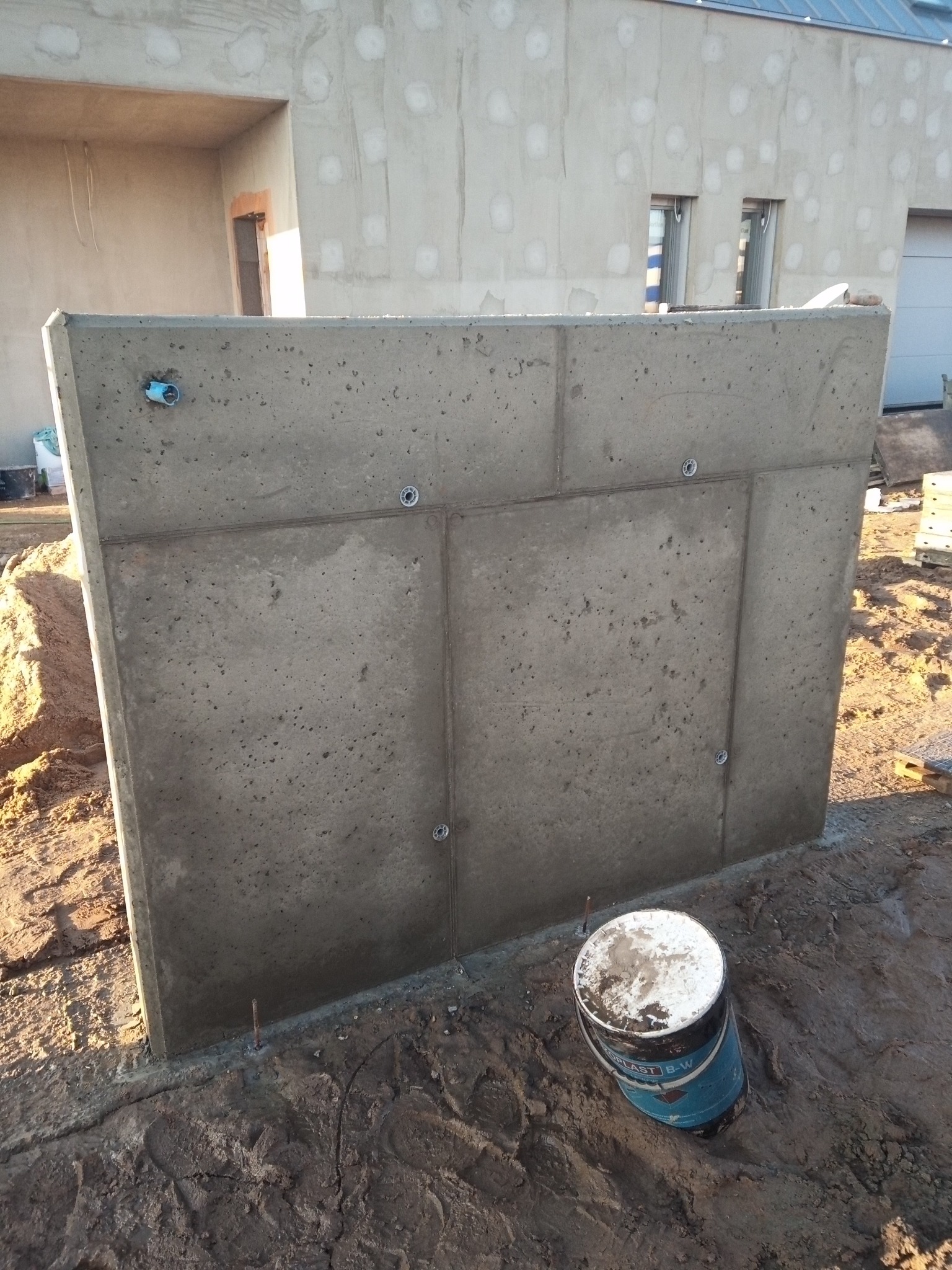 Betonowy fundament segmentowy z widocznymi elementami montażowymi w Dopiewie, na tle budynku w trakcie budowy. Widoczny kubeł z resztkami zaprawy.