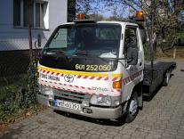 Laweta Toyota Dyna z numerem telefonu na karoserii, zaparkowana w Warszawie na tle drzew i budynku.