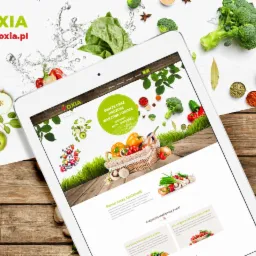 Tablet wyświetla stronę internetową firmy Oxia z owocami i warzywami, otoczony świeżymi produktami spożywczymi na białym tle z drewnianym akcentem.