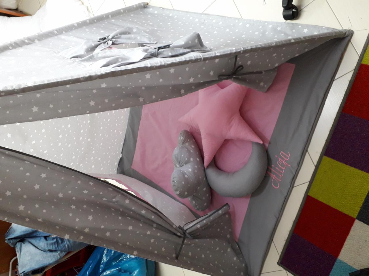 Dziecięcy namiot tipi z szarej tkaniny w białe gwiazdki, wewnątrz różowa mata z imieniem 'Alicja' oraz poduszki w kształcie gwiazdy, księżyca i chmurki.