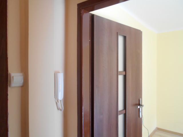 Brązowe drzwi wewnętrzne z przeszkleniem, zamontowane w odnowionym mieszkaniu w Górze Świętej Małgorzaty, widoczne na tle świeżo pomalowanej ściany z domofonem.