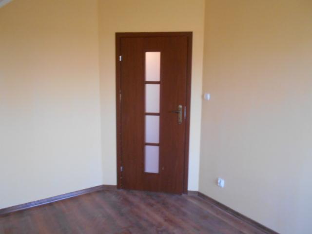 Brązowe drzwi wewnętrzne z trzema szybkami w nowo wyremontowanym pokoju z drewnianą podłogą i świeżo pomalowanymi ścianami na beżowo.