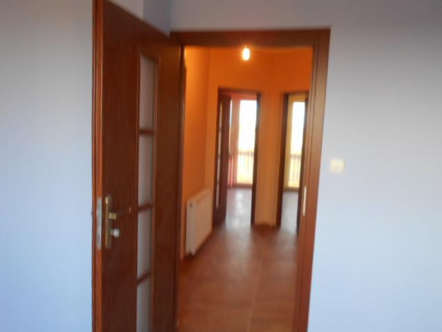 Otwarta drewniana dwuskrzydłowa drzwi z przeszkleniami, widok na wnętrze mieszkania z terakotą na podłodze i grzejnikiem.