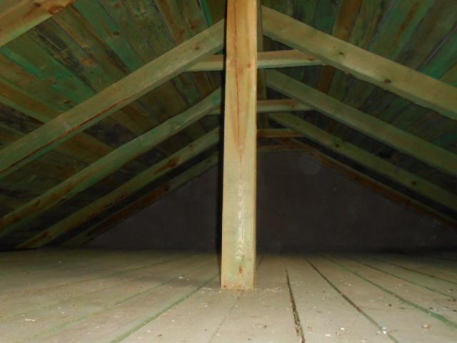 Surowe drewniane krokwie dachu poddasza, z widocznym słupem wspierającym i podłogą z desek, przygotowane do dalszych prac wykończeniowych.