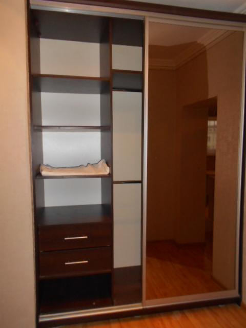 Wnętrze szafy przesuwnej z lustrem, widoczne półki i szuflady w kolorze ciemnego brązu, w tle parkiet.