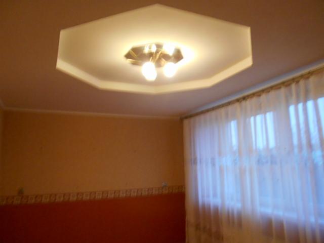 Pokój z pomarańczowymi ścianami, oświetlony ośmiokątną lampą sufitową i zasłoniętym oknem.