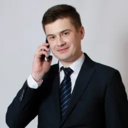 Uśmiechnięty mężczyzna w garniturze i krawacie w paski, rozmawia przez telefon, na jasnym tle.