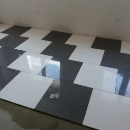 Układanie podłogi z płytek w szachownicę, biało-szare płytki, widoczne krzyżyki dystansowe i resztki zaprawy.