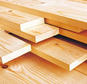 Stos świeżo obrobionych, jasnych desek sosnowych z widocznymi słojami drewna, ułożonych warstwami na podłożu z desek.