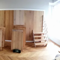 Ekspozycja paneli podłogowych i schodów w salonie, różne odcienie drewna, ułożone w jodełkę na podłodze, próbki schodów i panele pionowo na stojakach.