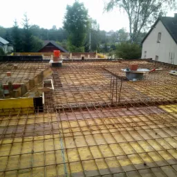 Zbrojenie stropu budynku jednorodzinnego na drewnianym szalunku, widoczne kominy wentylacyjne i okoliczna zabudowa.