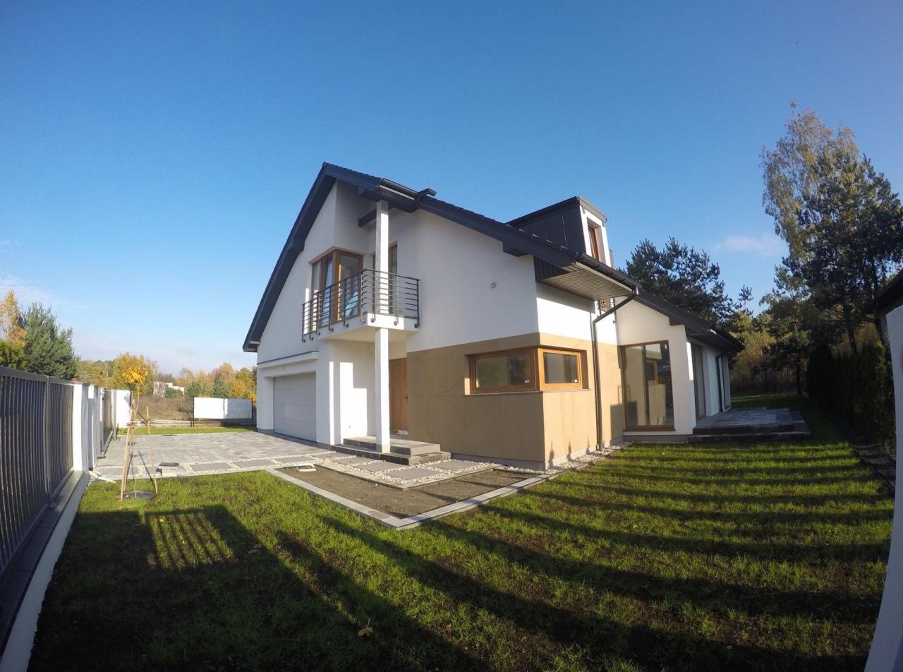 Nowoczesny dom jednorodzinny z szarą siatką ogrodzeniową, kostką brukową na podjeździe i świeżo założonym trawnikiem w słoneczny dzień.