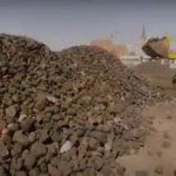 Żółta ładowarka nabiera węgiel z hałdy na placu składowym, widok z dołu.