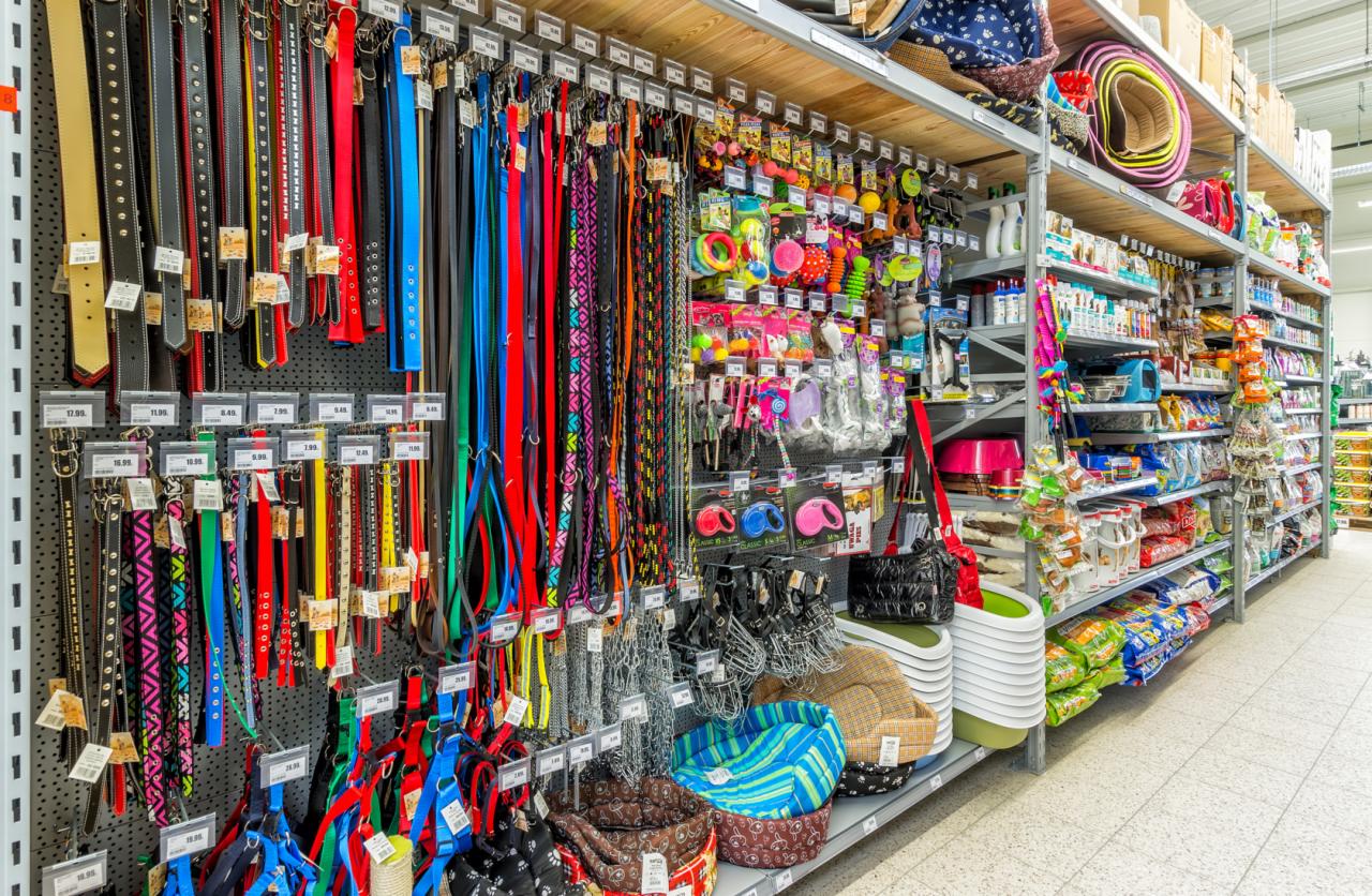 Szeroki kadr sklepowych półek z artykułami dla zwierząt: obroże, smycze, szelki, zabawki, legowiska, karmy i akcesoria do pielęgnacji, z widocznymi cenami.