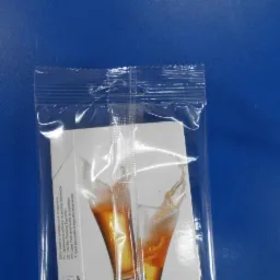 Przezroczyste, zgrzewane opakowanie foliowe zawierające kartonik z nadrukiem przedstawiającym kieliszek z napojem, widoczne tłumaczenia nazwy produktu na r&oacute;żne języki.