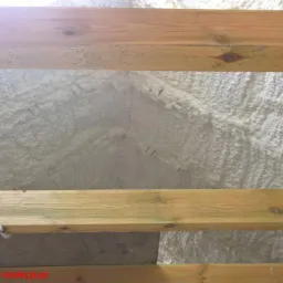 Poddasze ocieplone białą pianą natryskową, widoczne drewniane belki konstrukcyjne i przewód elektryczny, logo firmy STALMET w rogu.