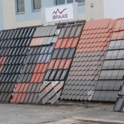Ekspozycja różnych modeli i kolorów dachówek ceramicznych marek Braas i Creaton na zewnątrz budynku.