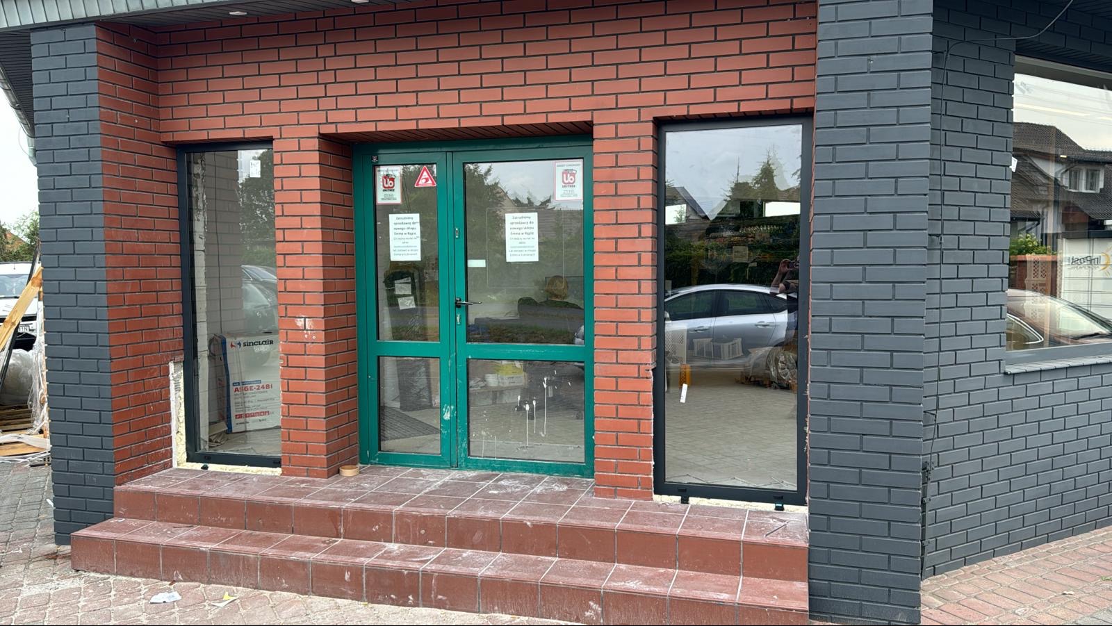 Nowo zamontowane okna i drzwi w budynku z cegły, widoczne ślady prac montażowych na schodach wejściowych.