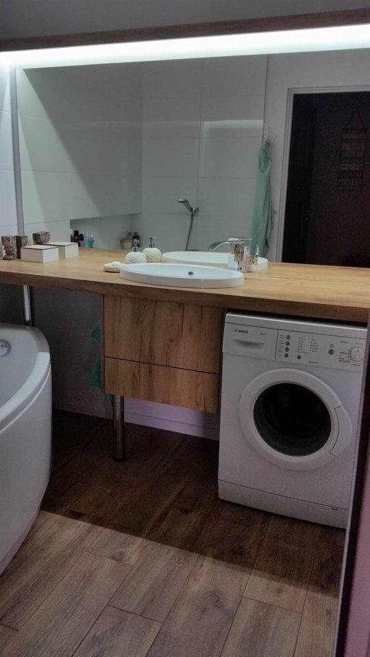 Nowoczesna aranżacja łazienki w Zduńskiej Woli z drewnianym blatem pod umywalką, pralką Bosch i podświetlanym lustrem.