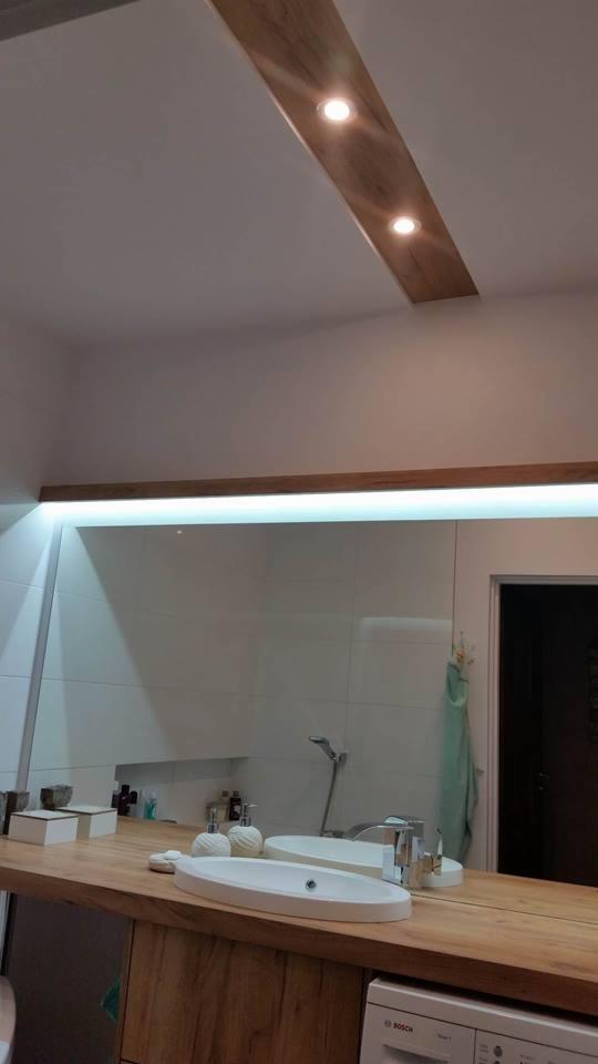Nowoczesna łazienka z drewnianym blatem, owalną umywalką nablatową, dużym lustrem z podświetleniem LED i wbudowanymi punktowymi lampami w suficie.