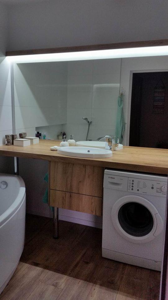 Nowoczesna łazienka z drewnianym blatem pod umywalką, pralką Bosch i podświetlanym lustrem, widok na kabinę prysznicową.