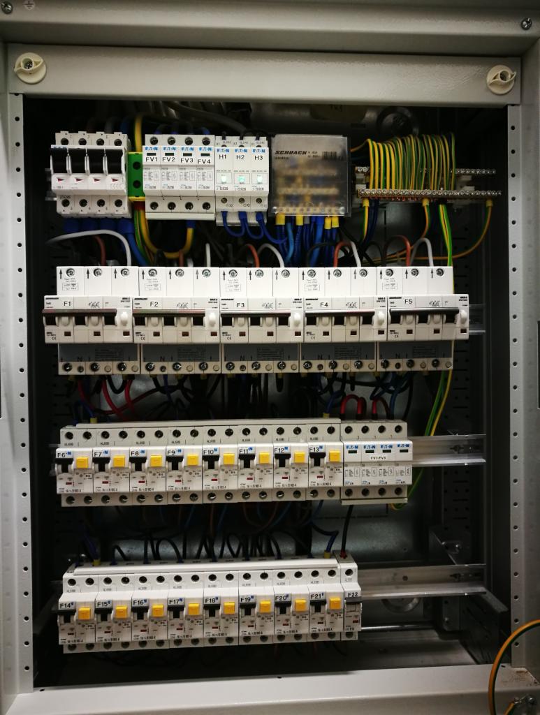 Wewnętrzny widok rozdzielnicy elektrycznej z bezpiecznikami i okablowaniem, widoczne oznaczenia F1-F22, FV1-FV4 oraz H1-H3.