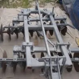 Metalowa brona talerzowa po renowacji, pokryta świeżą, szarą farbą. Widoczne ślady korozji na elementach roboczych.