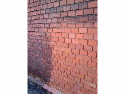 Częściowo oczyszczona, czerwona ściana z cegły. Po lewej stronie widoczny ciemny, zabrudzony obszar, kontrastujący z jaśniejszą, oczyszczoną prawą częścią.