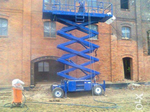 Prace przygotowawcze do odnowienia ceglanej elewacji budynku z użyciem podnośnika nożycowego i piaskarki z osprzętem ochronnym.