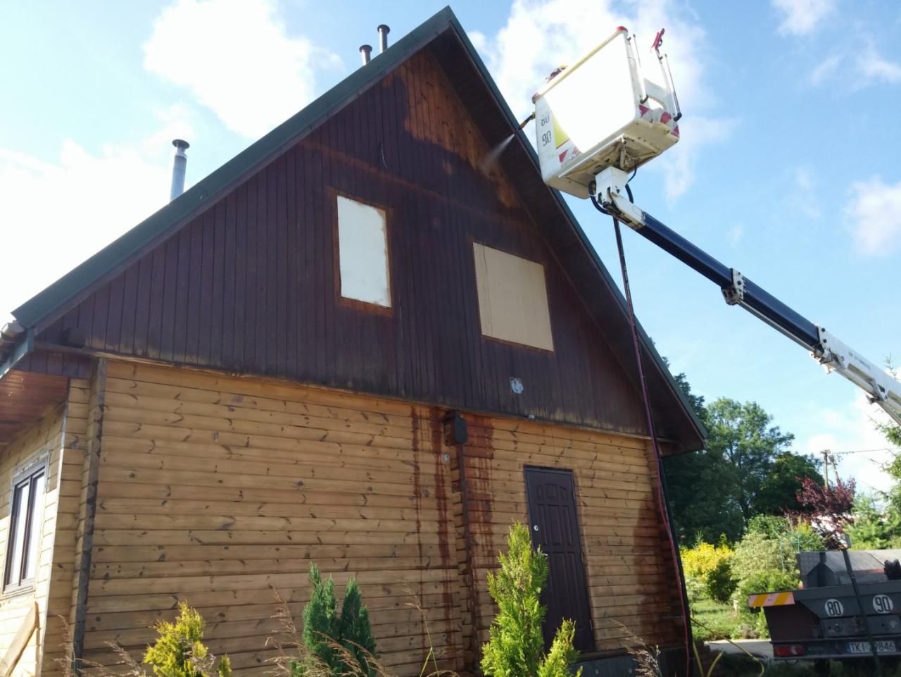Czyszczenie elewacji drewnianego domu z podnośnika koszowego; widoczne ślady spływającej wody i różnica w kolorze drewna przed i po czyszczeniu.