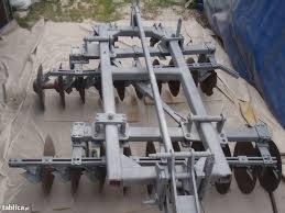 Metalowa brona talerzowa po renowacji, pokryta świeżą, szarą farbą. Widoczne ślady korozji na elementach roboczych.