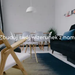 Jasne wnętrze z drewnianym krzesłem na pierwszym planie, w tle stół z krzesłami, sofa i dekoracje ścienne.