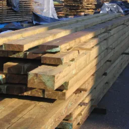 Stos impregnowanej tarcicy budowlanej ułożonej na zewnątrz, widoczne charakterystyczne zielonkawe ślady impregnatu na końcach desek.