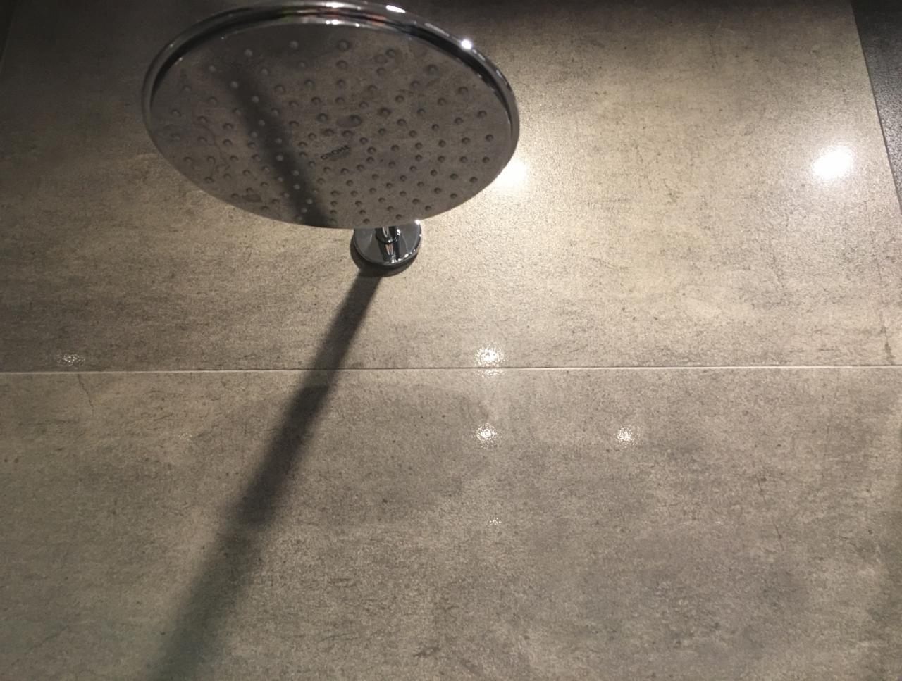 Zamontowana chromowana deszczownica Grohe na szarej, matowej ścianie z płytek, widoczne krople wody.