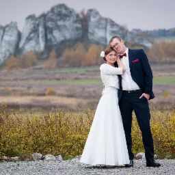 Para młoda w jesiennej scenerii z wapiennymi skałami w tle, ona w białej sukni i bolerku, on w granatowym garniturze z bordową muchą.