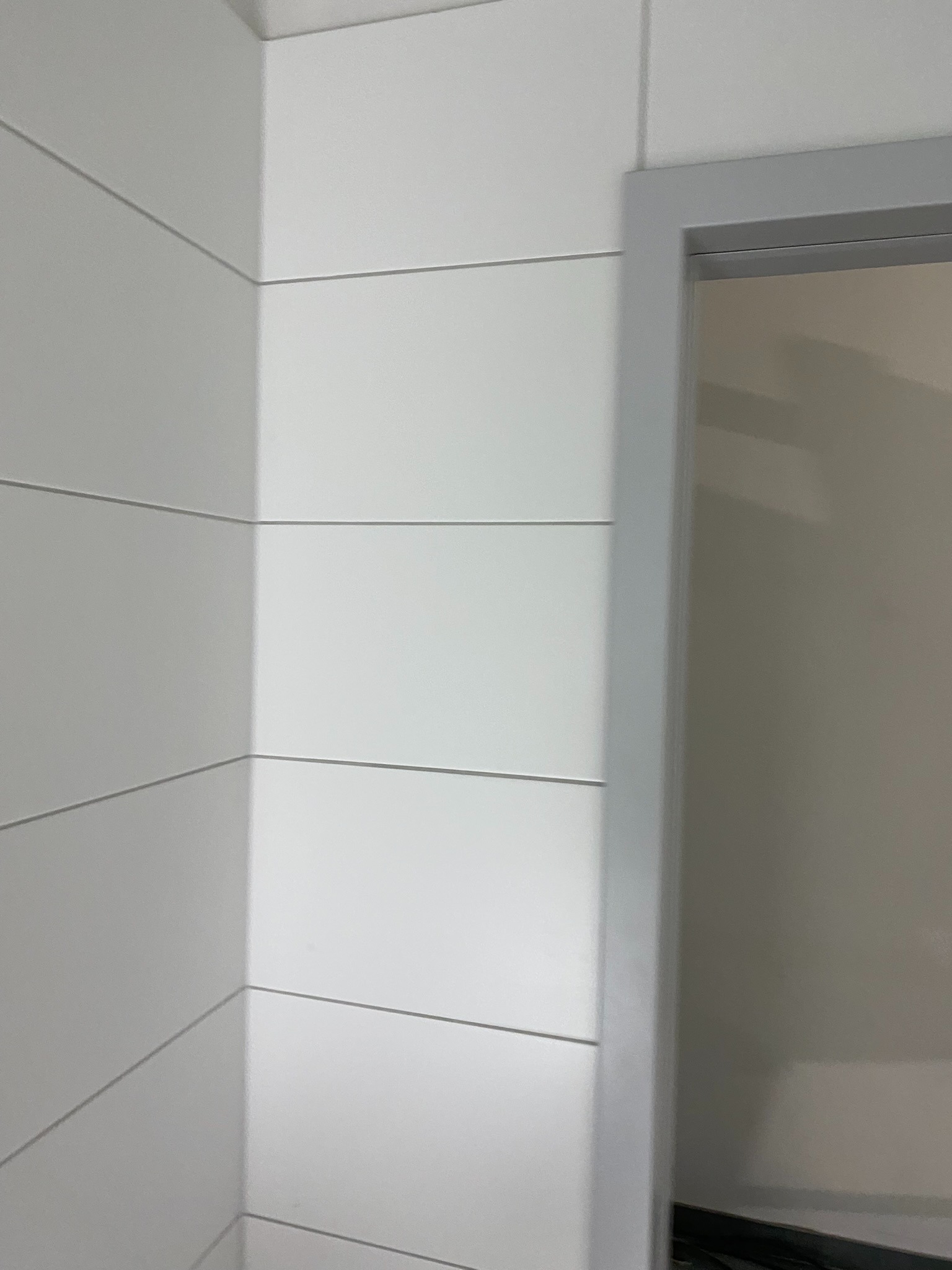 Ściana wykończona białymi panelami boazeryjnymi w Ostrzeszowie, widoczny narożnik i fragment ościeżnicy drzwiowej.