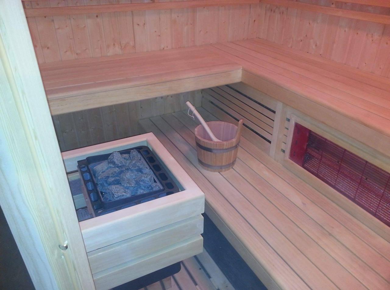 Wnętrze drewnianej kabiny z piecem na kamienie i drewnianym wiadrem z chochlą, oświetlone ciepłym światłem.