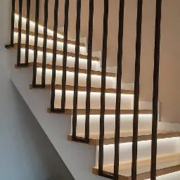 Nowoczesne schody z drewnianymi stopniami, podświetleniem LED i czarną, minimalistyczną balustradą. W tle widoczny stolik z ubraniami.