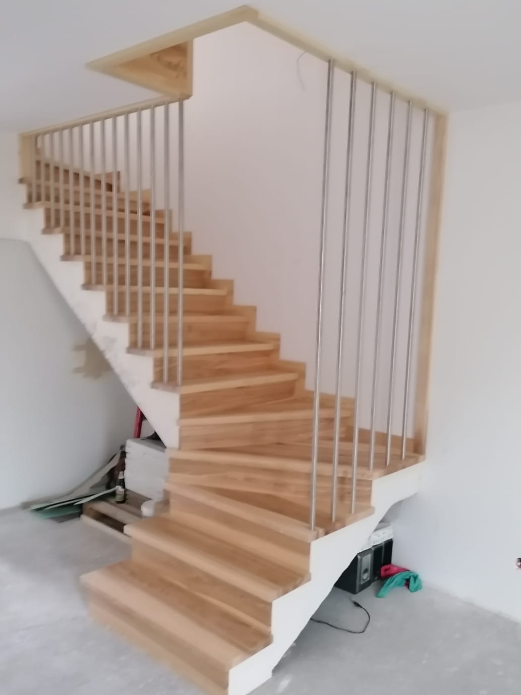 Spiralne schody z jasnego drewna z metalowymi balustradami w nowym domu, widoczne elementy wykończeniowe i narzędzia