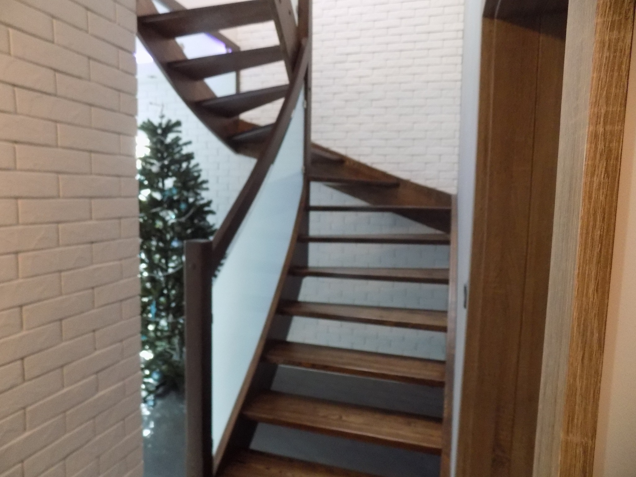 Spiralne schody z drewna z białymi panelami bocznymi, widok z dołu na tle białej ceglanej ściany i choinki
