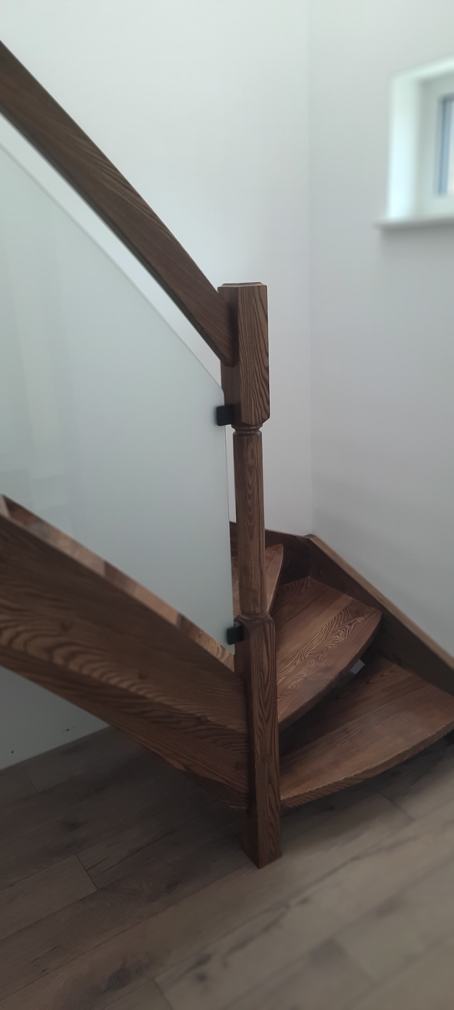 Kąt ujęcia na drewniane schody z balustradą ze szkła, widoczne elementy mocujące szkło do słupka