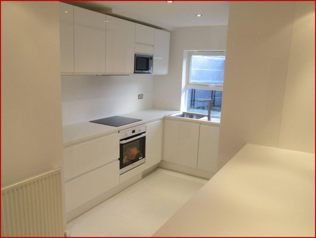 Jasna kuchnia z białymi, lakierowanymi szafkami, piekarnikiem z piekącym się kurczakiem i oknem nad zlewem, widok z boku na blat.