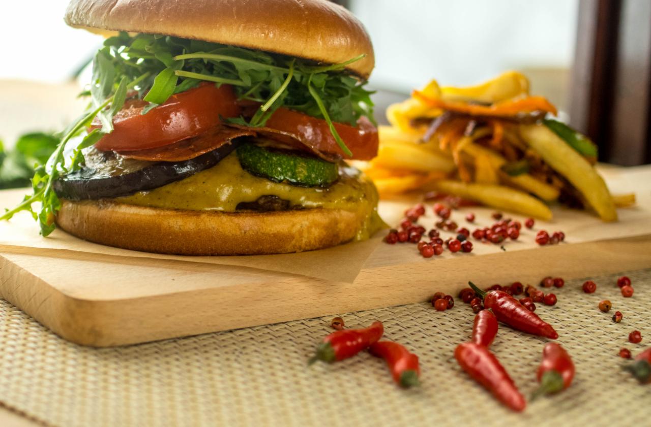 Wegański burger z grillowanym bakłażanem, cukinią, pomidorem i rukolą, podany z frytkami i czerwonym pieprzem na drewnianej desce.