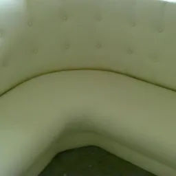 Fragment narożnika tapicerowanego jasną skórą ekologiczną, z charakterystycznym pikowaniem i guzikami na oparciu.