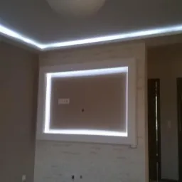 Pokój z zamontowanym oświetleniem LED w suficie i wnęce na ścianie, drabina oparta o ścianę, widoczne gniazdka elektryczne.