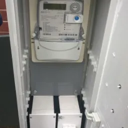 Otwarta skrzynka z licznikiem energii elektrycznej i zabezpieczeniami, widoczne przewody.